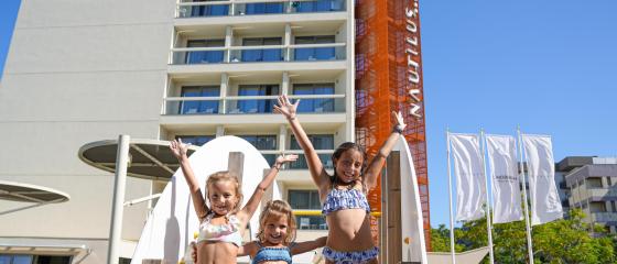 Bambini felici in costume giocano davanti a un hotel moderno e luminoso.