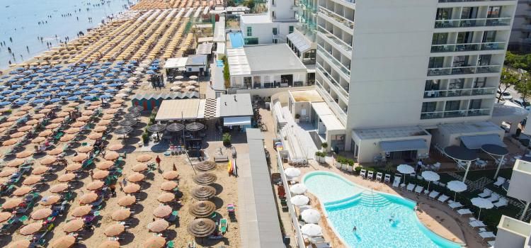 Spiaggia affollata, ombrelloni colorati, hotel moderno e piscina invitante, estate in pieno.