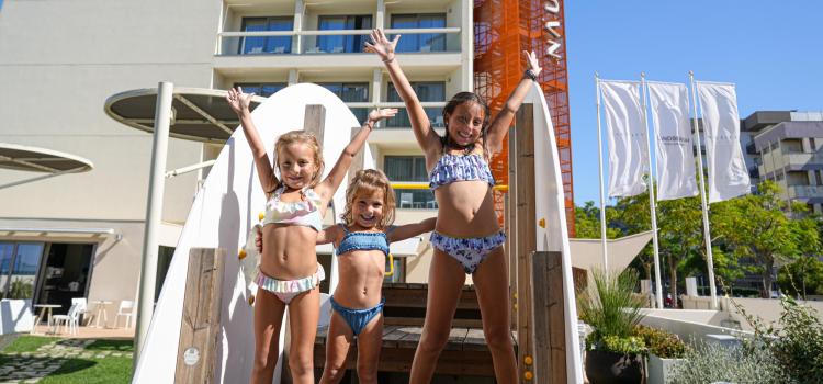 Bambini felici in costume giocano davanti a un hotel moderno e luminoso.